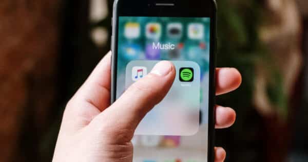 Eine Hand tippt auf einem iPhone-Display auf die App-Logos von Apple Music und Spotify