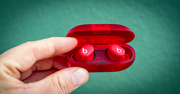 Eine Hand hält die Beats Solo Buds in Transparent-Rot vor einem grünen Hintergrund