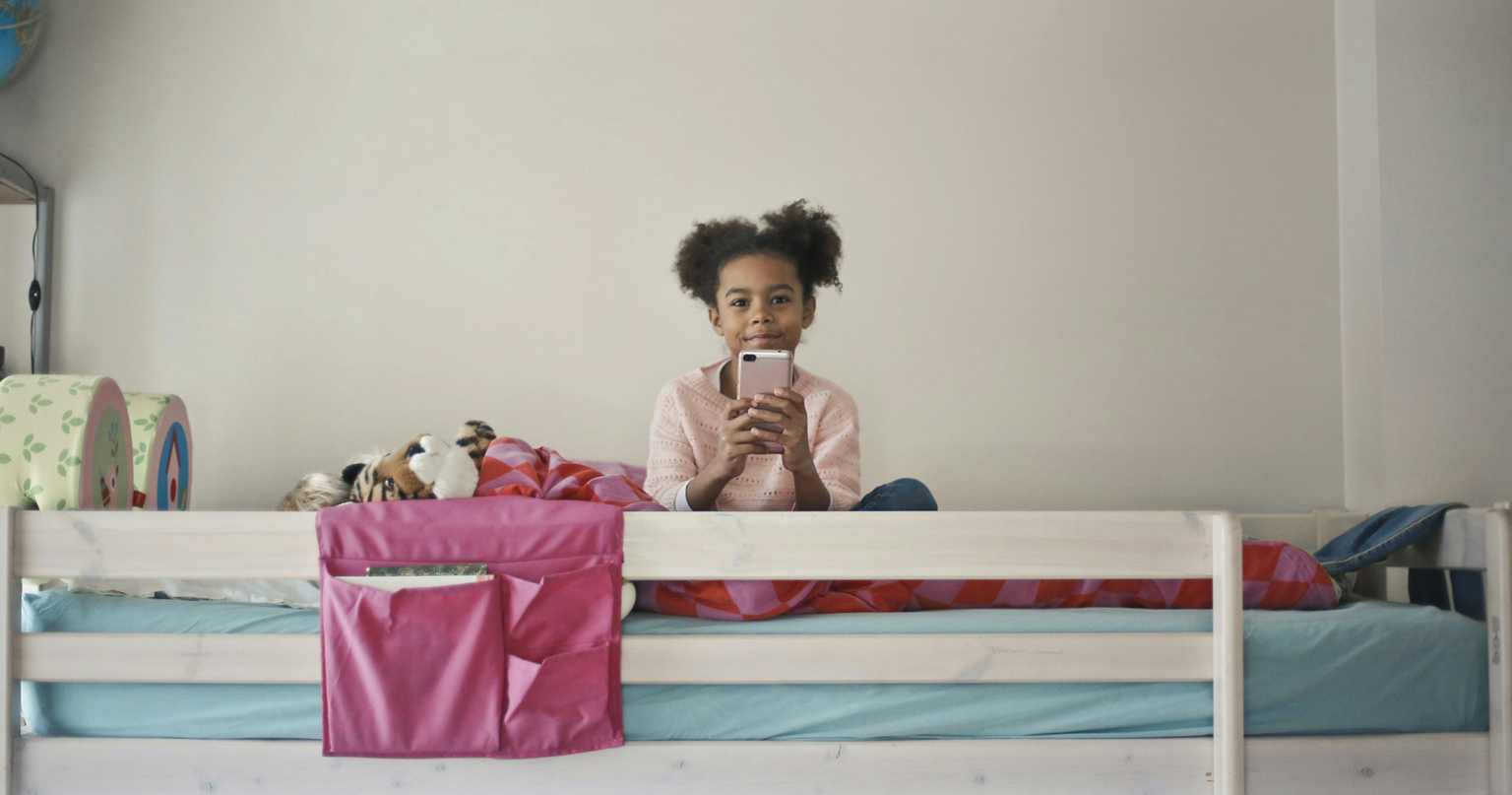 Ein Kind sitzt auf seinem Hochbett und hat ein Handy in der Hand