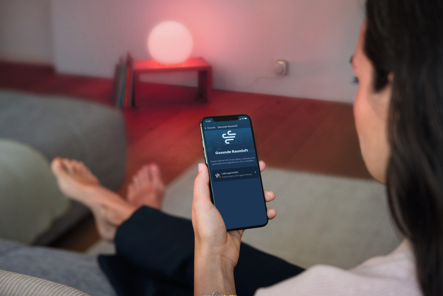 Frau sieht auf Handy dass es laut Bosch Smart Home Zeit zum Lüften ist. Eine rote Leuchte warnt auch. Symbolbild für Automatiken von Bosch Smart Home im Test