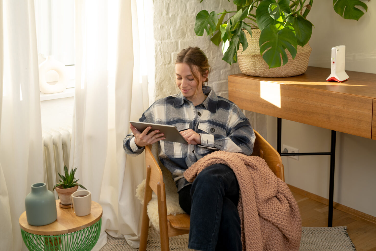 Frau bedient auf dem Tablet ihr Fritz!Box Smart Home mit dem WLAN-Router daneben auf der Kommode