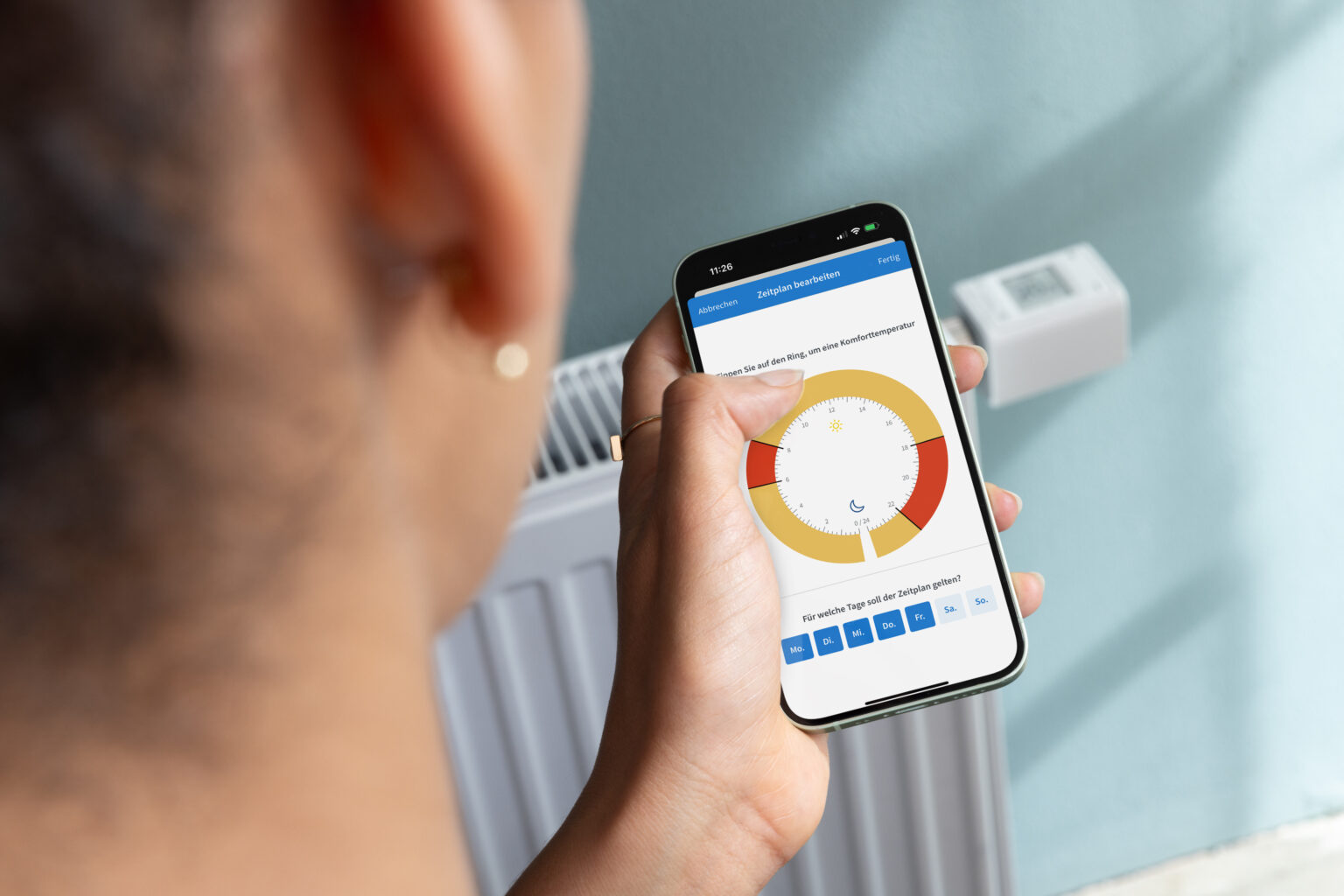 Mensch hält Fritz!App auf Smartphone vor ein AVM-Heizkörperthermostat