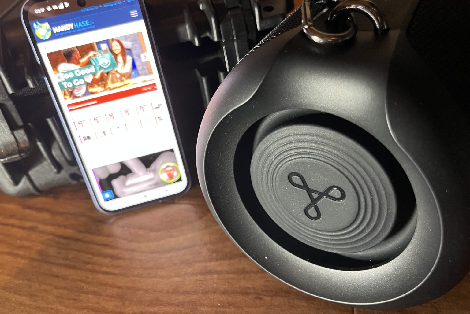 Ein großer Treiber bietet tiefe und kräftige Bässe. Daneben ein Smartphone als Größenvergleich.