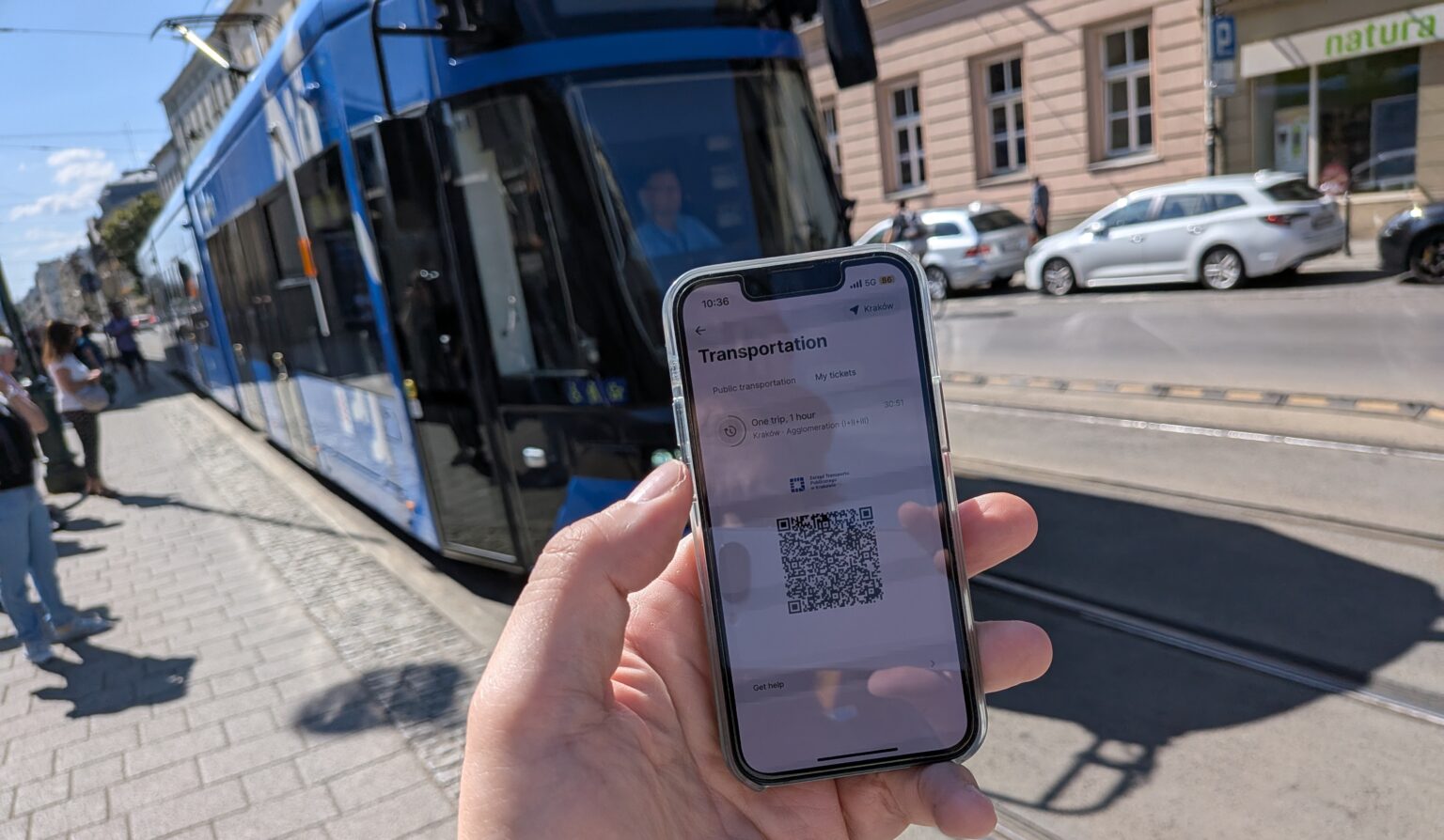 Revolut-App mit ÖPNV-QR-Code vor einer blauen Straßenbahn gehalten.