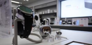 Blick in den Xiaomi-Store im Hintergrund mit Nahaufnahme auf eine Smartwatch und ein Ohrhörer-Case (freigestellt).