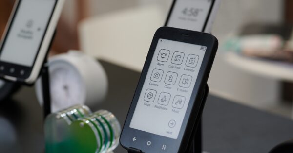 Freigestelltes Kompakt in Schwarz vor weiteren zwei Kompakt-Geräten im Hintergrund. Mit Kachel-Oberfläche für Apps sichtbar.