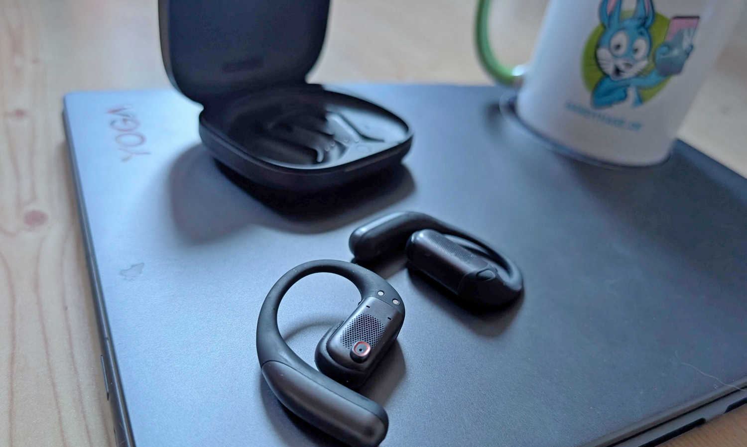 Shokz Open Fit 2 Pro im Test - Detailaufnahme auf grauem Hintergrund mit Handyhase-Tasse und Ladeschale