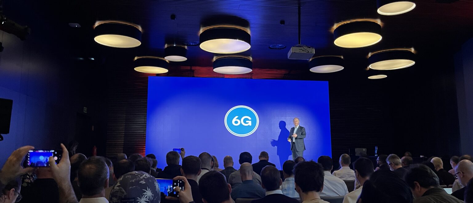 Bühne von Qualcomm mit 6G-Logo auf dem Bildschirm und Präsentator.