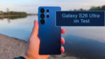 Hand hält Smartphone, sichtbar ist Rückseite des Samsung Galaxy S26 Ultra mit See im Hintergrund und Text